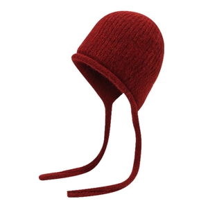 Dark red wool knit beanie with braided earflaps and textured vertical stripes on white background