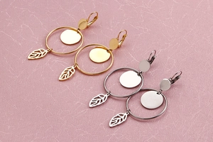 Detail view of gold and silver hoop earrings with leaf charms on a textured background