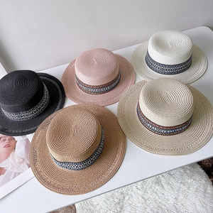 Cappelli di paglia a cima piatta in vari colori con nastri boho su tavolo bianco