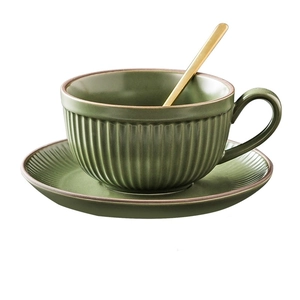 Detail of dark green matte ceramic coffee cup with vertical stripes and gold spoon