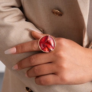 Close-up of a large round red enamel ring with gold trim worn with a khaki suit