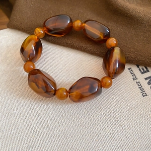 Close-up of brown acrylic beaded bracelet with irregular amber resin texture on fabric