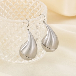 Detailed view of silver teardrop earrings with a brushed metal finish on fabric