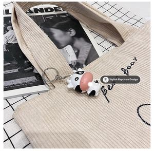 Detail of beige corduroy tote bag featuring blue embroidery and a cow-shaped charm