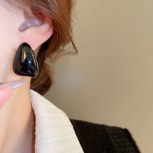 Close-up of black geometric triangle earring with gold trim on model's ear