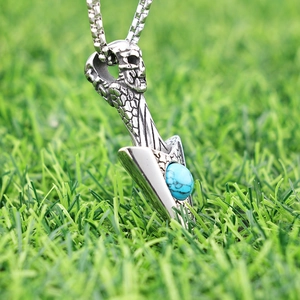 Punk silver skull dagger pendant with turquoise stone on green grass background
