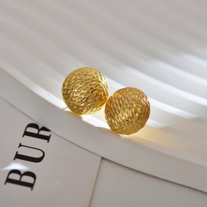 Close-up of golden irregular spherical earrings with detailed geometric 3D texture