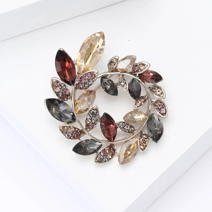 Detail shot of a crystal olive branch wreath brooch on a minimalist white platform