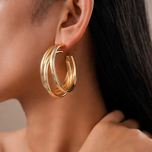 Close-up of a large gold multi-layered C-shaped hoop earring worn on a model ear