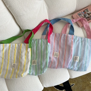 Détail de quatre sacs fourre-tout rayés en toile aux couleurs vives sur un canapé blanc