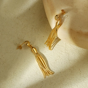 Macro shot of gold-plated octopus tentacle tassel earrings on a textured stone surface