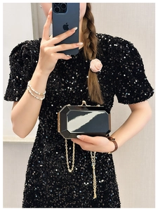 Macro detail of black geometric acrylic clutch bag with gold chain and metal frame