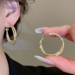 Detailed macro view of gold-plated hoop earrings featuring fine textured horizontal grooves