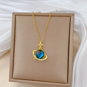 Macro shot of gold planet necklace with blue cosmic stone and diamond halo on beige box