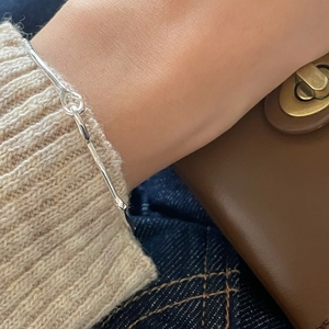 Detail of minimalist S925 sterling silver buckle bracelet on wrist with cozy knitwear