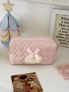 Pink quilted makeup bag with heart stitching, bow detail and lace trim on white desk