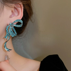 Detailed close-up of teal rhinestone bow earrings with elegant fringe on ear lobe