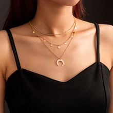 Close-up of layered gold necklace featuring moon pendant and discs on female model neck