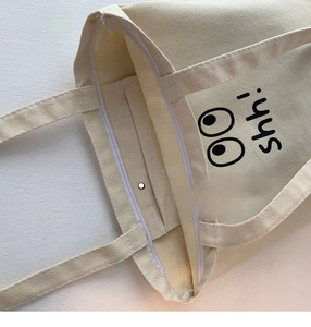 Detalle del bolso tote de lona beige con cremallera y bolsillo interior para móvil