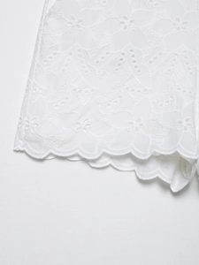 Dettaglio del ricamo floreale bianco e motivo traforato sull'orlo smerlato dei pantaloni
