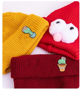 Detail of colorful knit beanies featuring cartoon cactus embroidery and plush big eyes