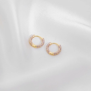Macro shot of gold-plated hoop earrings with lavender enamel inlay on silk background