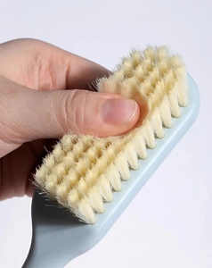 Close-up of soft beige bristles being pressed to show flexibility on a blue cleaning brush