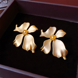 Macro shot of matte golden vintage flower earrings inside a premium black velvet jewelry box