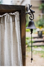 Detail of vintage cast iron garden doorbell with bird and leaf carving on wooden post