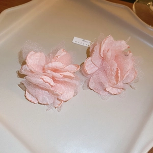 Close-up of pink tulle flower earrings with pearl accents on a white decorative plate