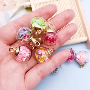 Handmade glass bottle charms with colorful star sequins and fruit slices held in hand