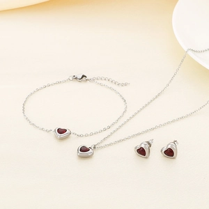 Détail d'un ensemble de bijoux coeur en argent avec pierres rouges sur fond texturé