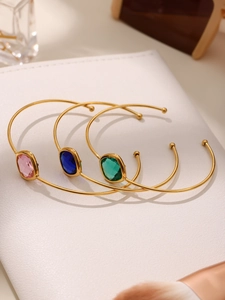 Close-up of gold stainless steel open bangles with pink blue and emerald glass gems