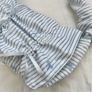 Detail of blue and white striped fabric bag with satin bows and embroidered patterns