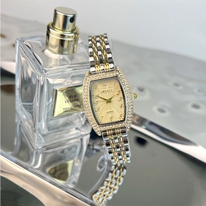 Detail of tonneau emerald quartz watch with crystal bezel on a silver reflective tray