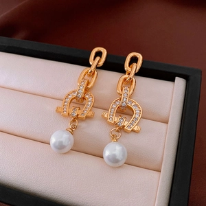 Detail of golden horseshoe earrings with zirconia stones and hanging white pearls