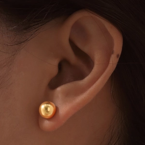 Close-up of a gold-finish round ball stud earring on earlobe for a minimalist jewelry look