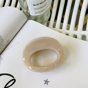 Detail of minimalist cream oval hair claw clip shown against a stylish lifestyle backdrop