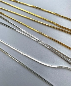 Close-up of gold and silver layered snake bone necklaces with high-shine metallic finish