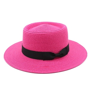 Close-up of fuchsia woven straw hat with black ribbon detail and flat top crown