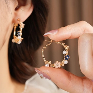 Macro detail of vintage gold hoop earrings with enamel flowers and delicate white pearls