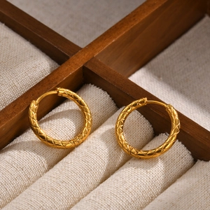 Macro view of gold-plated stainless steel hoop earrings with engraved diamond pattern textures
