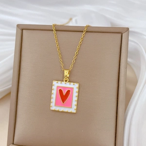 Close-up of gold square pendant with pink center and red heart on white fabric