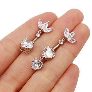 Vue détaillée de piercings de nombril en zircon cœur et rond tenus entre les doigts