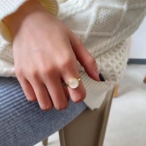 Detail of a minimalist gold ring with cat's eye stone worn on a finger over a white sweater