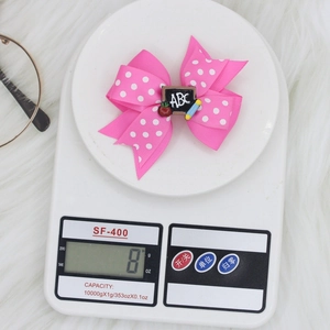 Detail showing back-to-school pink polka dot bow hair clip weighing 8 grams on a digital scale