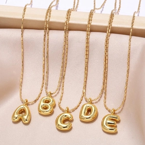 Gold bubble alphabet pendants A-E on delicate chains over pink silk fabric