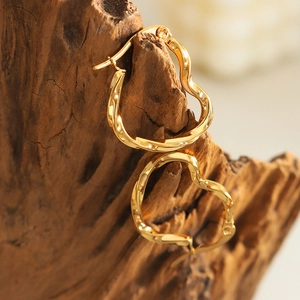 Polished golden heart shaped hoop earrings with elegant twisted texture on wood