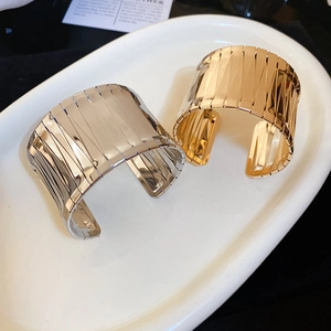 Detailed macro view of wide open metal bangles featuring vertical striped groove texture