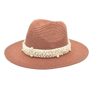 Detail of a brown woven straw fedora featuring a white ribbon adorned with faux pearls